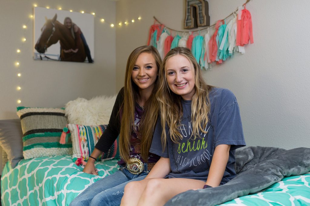 Two female students sitting together on a bed in a dorm room
